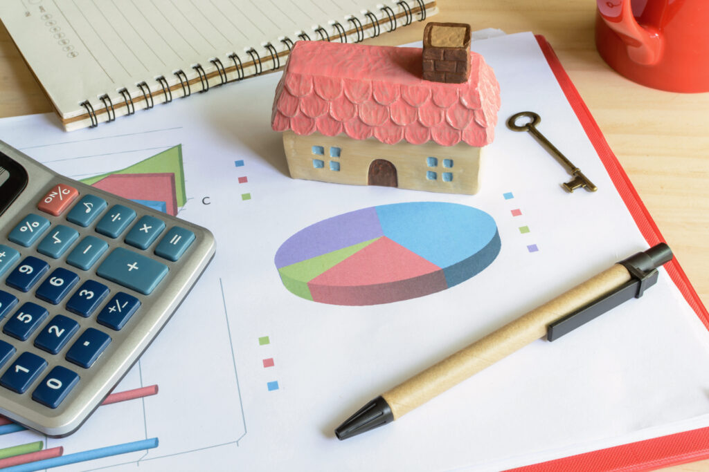 Home finance concept with miniature house next to a calculator and a pen on top of a graph